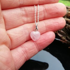small pink rose quartz heart pendant on sterling silver chain. held in the hand.